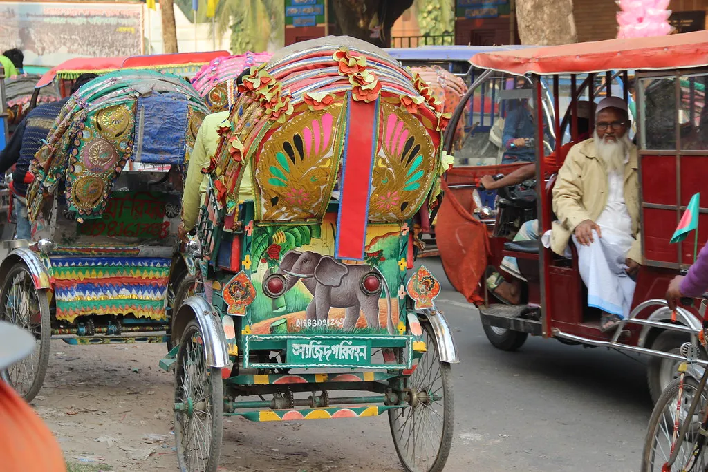 Painted cycle rickshaws waiting on a busy Dhaka street